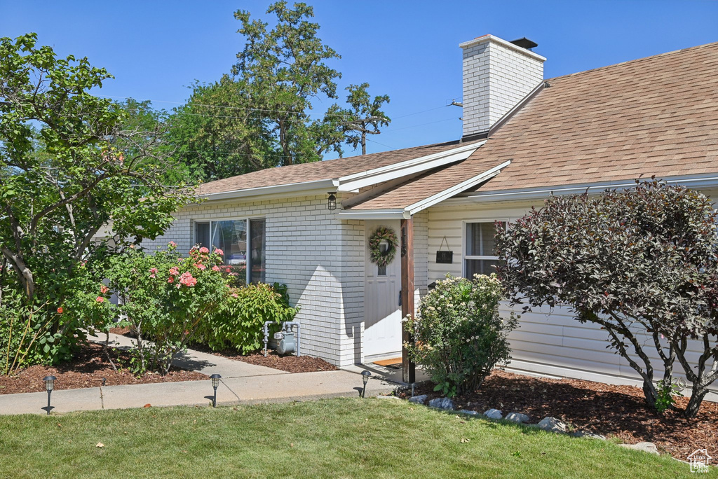 Property entrance with roof with shingles, a chimney, a yard, and brick siding