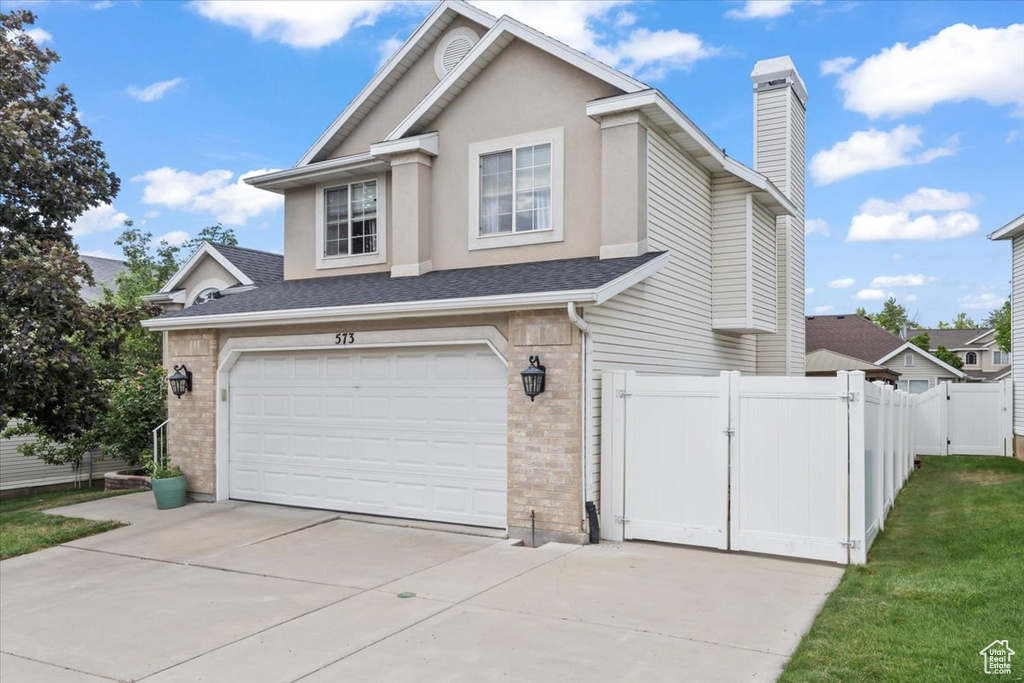 Traditional-style home featuring a gate, a garage, driveway, and brick siding