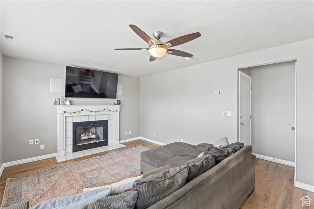Living room featuring a ceiling fan, wood finished floors, and a tiled fireplace