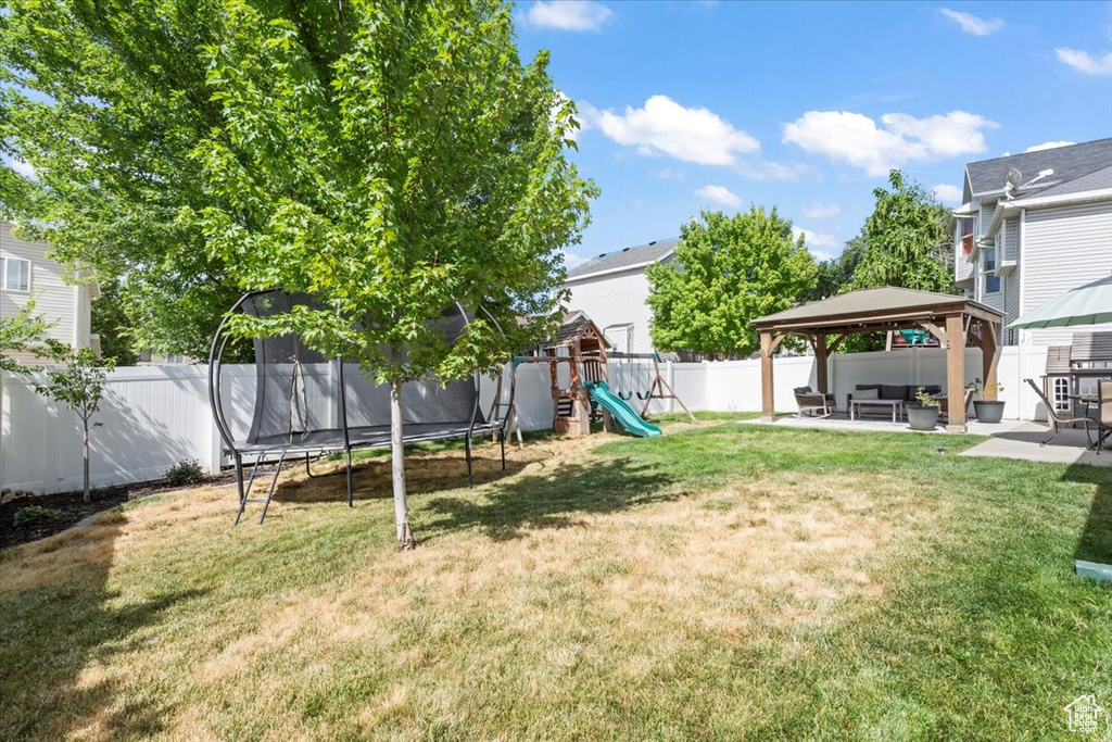 Fenced backyard featuring a trampoline, a gazebo, a playground, and a patio