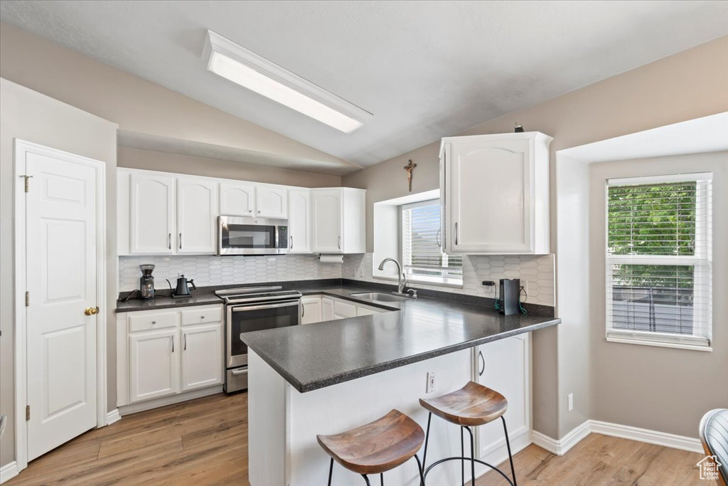 Kitchen featuring stainless steel appliances, a kitchen breakfast bar, white cabinetry, and vaulted ceiling