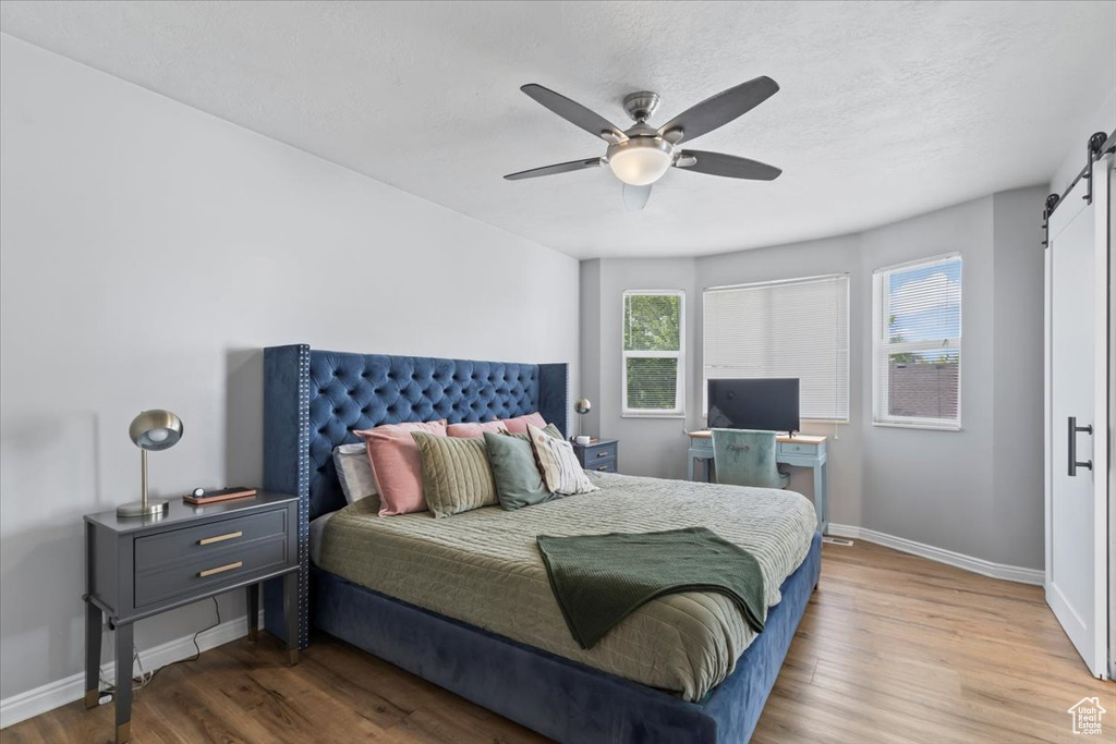 Bedroom featuring a barn door, wood finished floors, and a ceiling fan