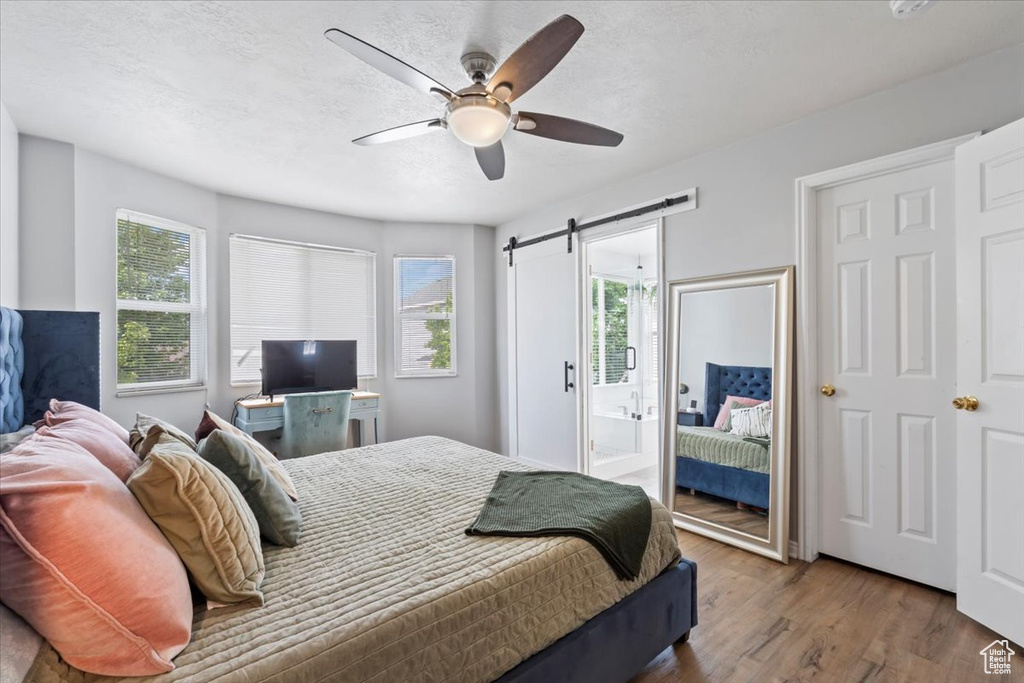 Bedroom with a barn door, wood finished floors, a ceiling fan, and ensuite bath