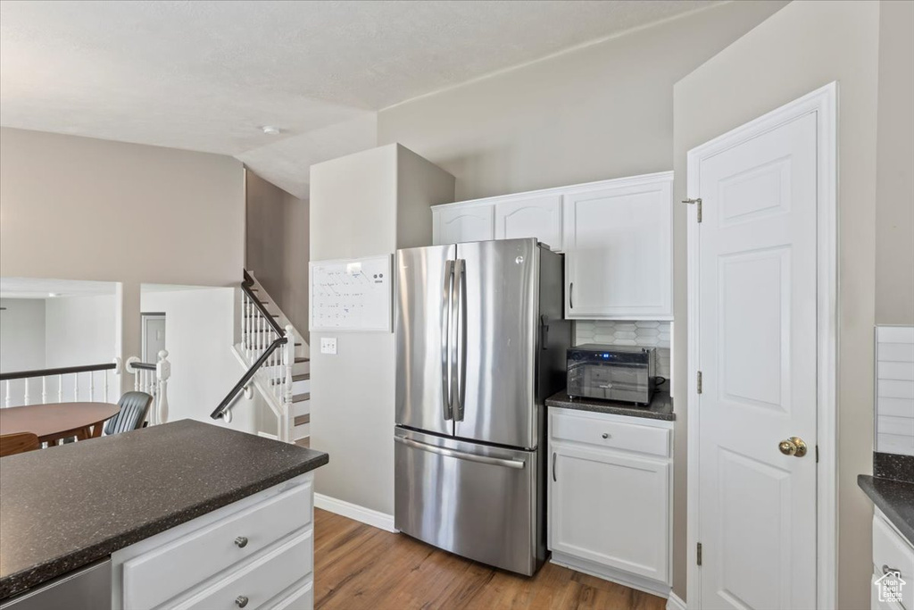 Kitchen with freestanding refrigerator, dark countertops, light wood-style flooring, white cabinetry, and decorative backsplash