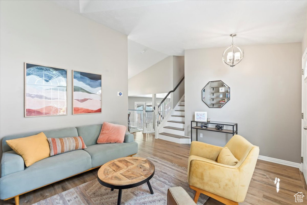 Living room with stairway, wood finished floors, a chandelier, and high vaulted ceiling