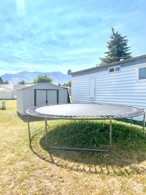 View of green lawn featuring a trampoline, a mountain view, and a shed