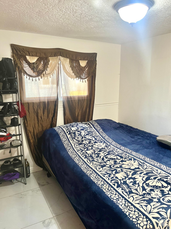 Bedroom with a textured ceiling and marble look tile flooring