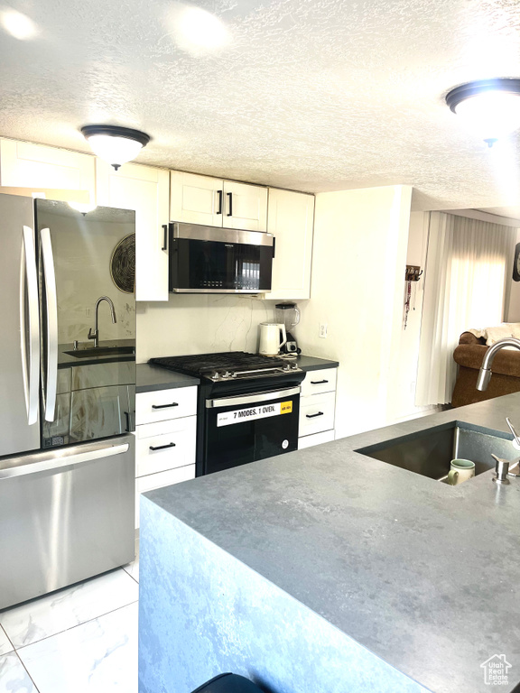 Kitchen featuring stainless steel appliances, white cabinetry, dark countertops, a textured ceiling, and light marble finish flooring