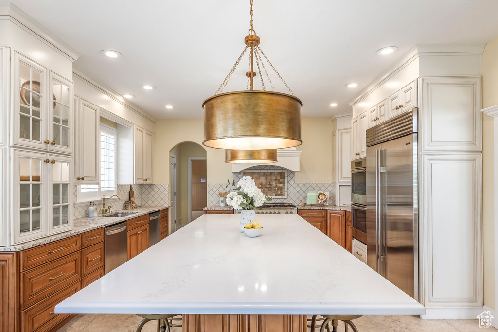 Kitchen featuring a kitchen breakfast bar, appliances with stainless steel finishes, brown cabinets, arched walkways, and recessed lighting