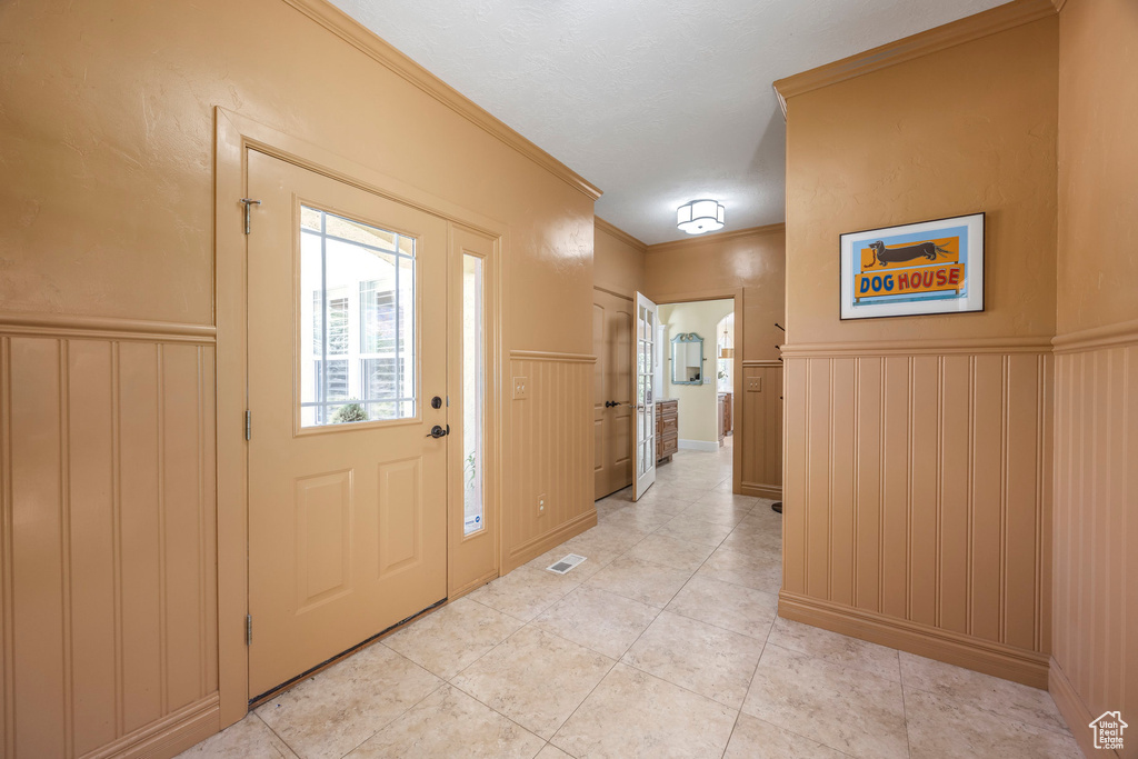Foyer with wainscoting, ornamental molding, light tile patterned floors, and a decorative wall