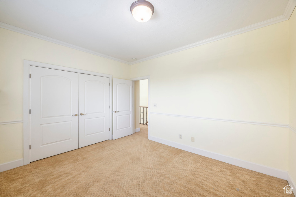 Unfurnished bedroom with crown molding, light carpet, and a closet