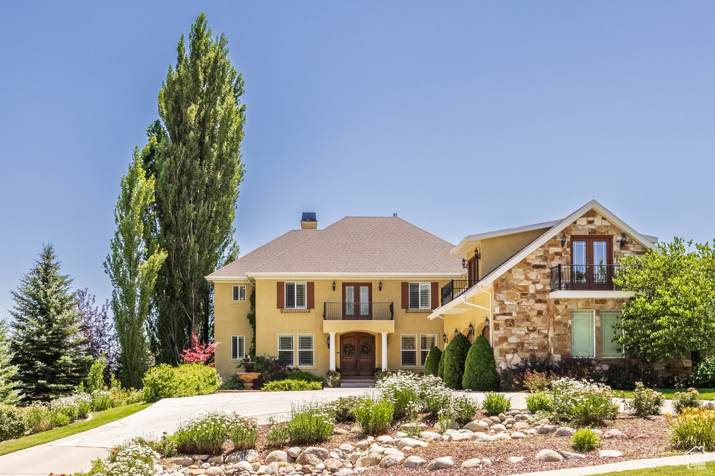 View of front of house with french doors, a balcony, stone siding, driveway, and stucco siding