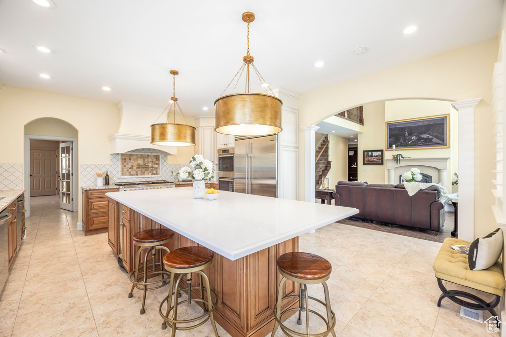 Kitchen with appliances with stainless steel finishes, arched walkways, custom range hood, light countertops, and backsplash