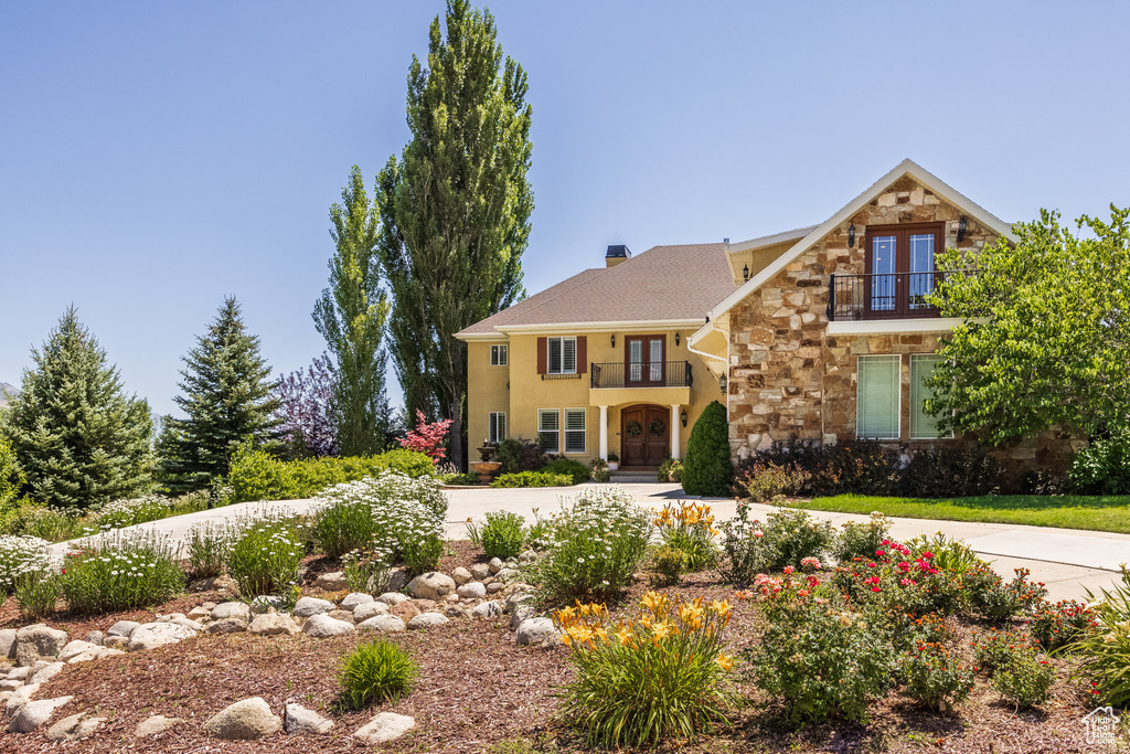 View of front of house featuring french doors, a balcony, stone siding, and stucco siding