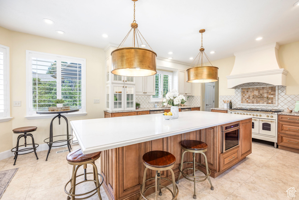Kitchen featuring range with two ovens, custom exhaust hood, light countertops, decorative backsplash, and a spacious island