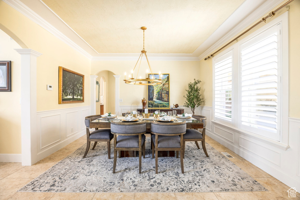 Dining room featuring arched walkways, a chandelier, a decorative wall, a wainscoted wall, and ornamental molding