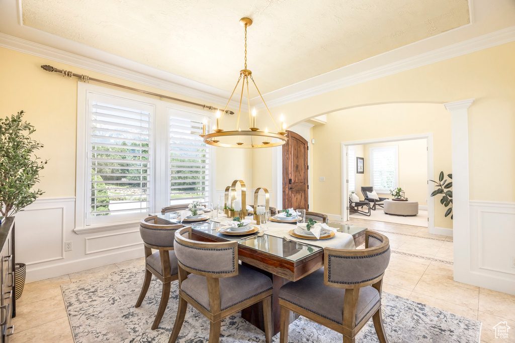 Dining area featuring arched walkways, a chandelier, a wainscoted wall, ornamental molding, and light tile patterned floors
