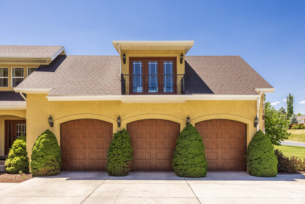 View of front of property with stucco siding, a balcony, roof with shingles, and a garage