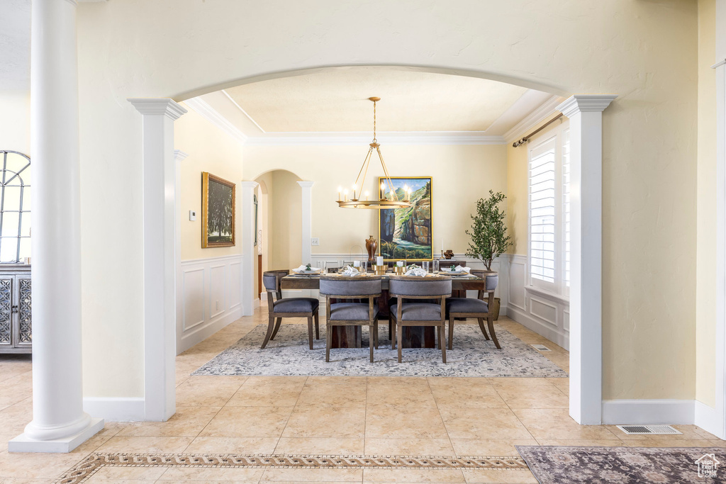 Tiled dining room featuring arched walkways, crown molding, a decorative wall, a wainscoted wall, and a chandelier