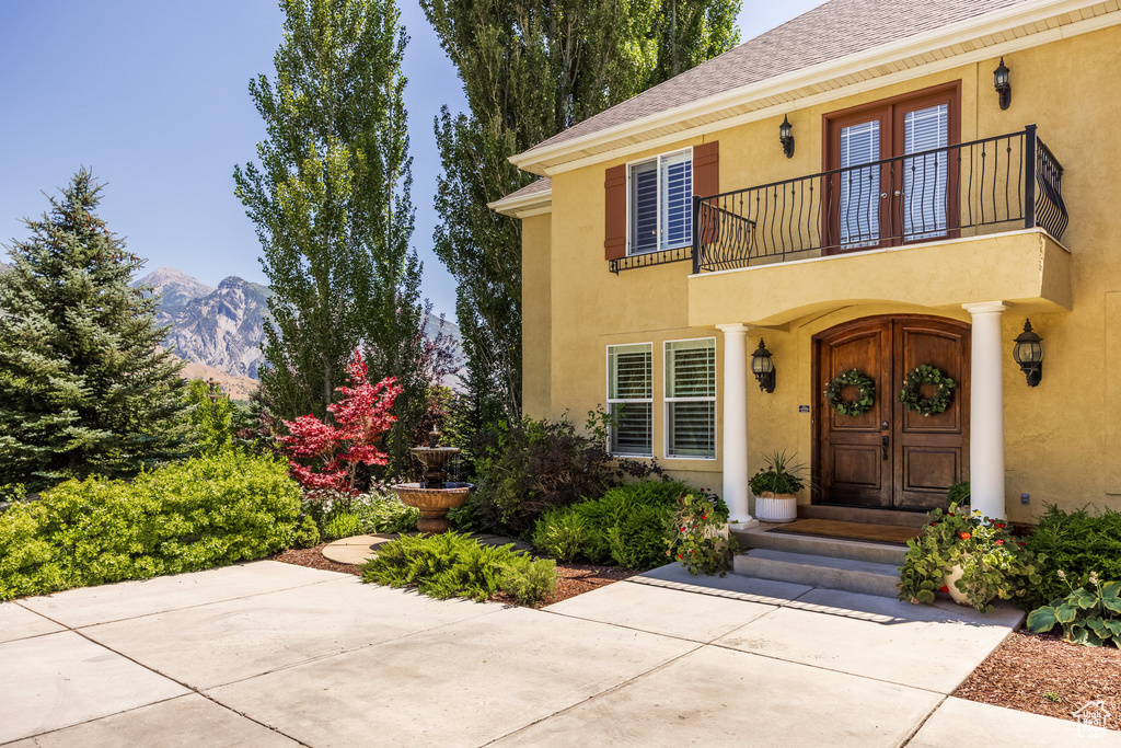 View of exterior entry featuring a balcony, stucco siding, a mountain view, a shingled roof, and french doors