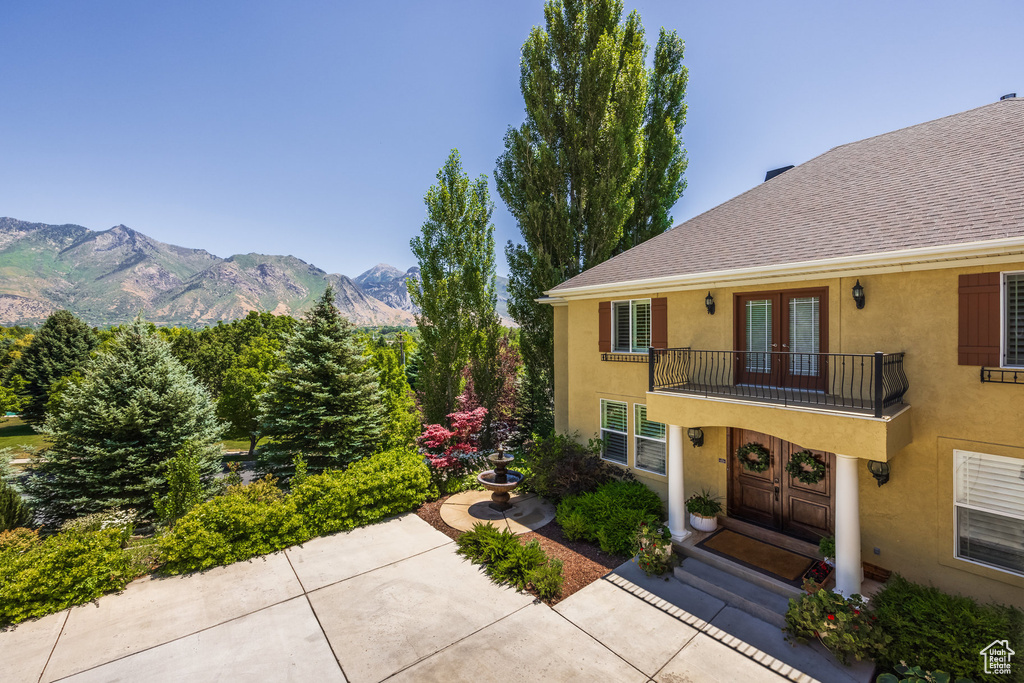 View of front of property featuring french doors, a balcony, stucco siding, a mountain view, and a shingled roof