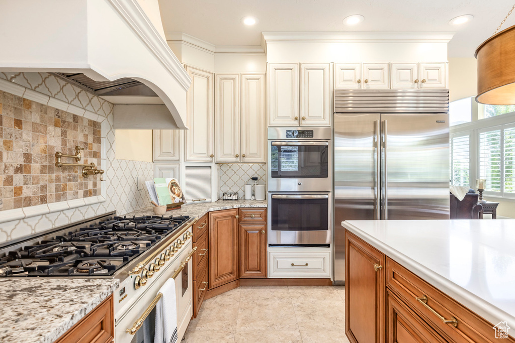 Kitchen with high end appliances, brown cabinetry, tasteful backsplash, and light tile patterned flooring