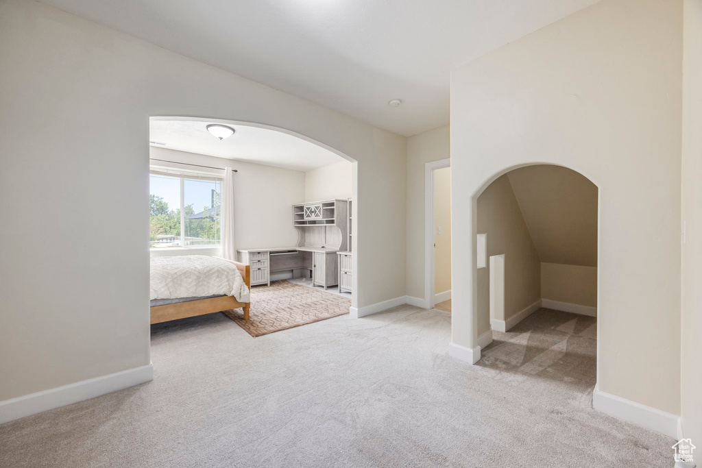 Unfurnished bedroom with carpet floors, arched walkways, and vaulted ceiling