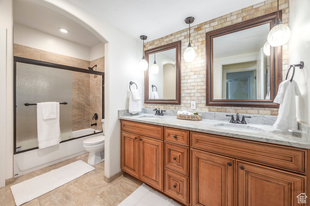 Full bath with double vanity, combined bath / shower with glass door, and decorative backsplash