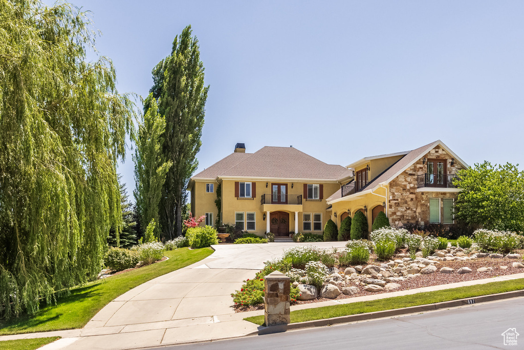 View of front of house featuring a balcony, curved driveway, stucco siding, stone siding, and a chimney