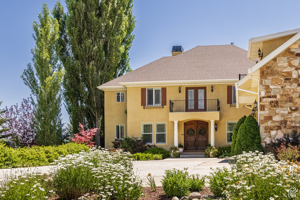 View of front facade with french doors, a balcony, stucco siding, a chimney, and stone siding