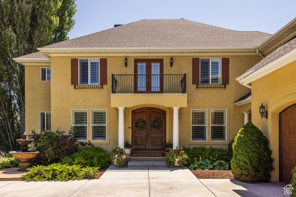 Property entrance with a balcony, french doors, stucco siding, and a shingled roof