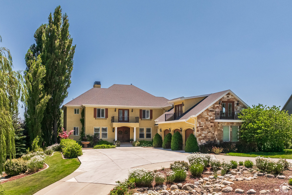 Mediterranean / spanish home with a balcony, stone siding, curved driveway, stucco siding, and a chimney