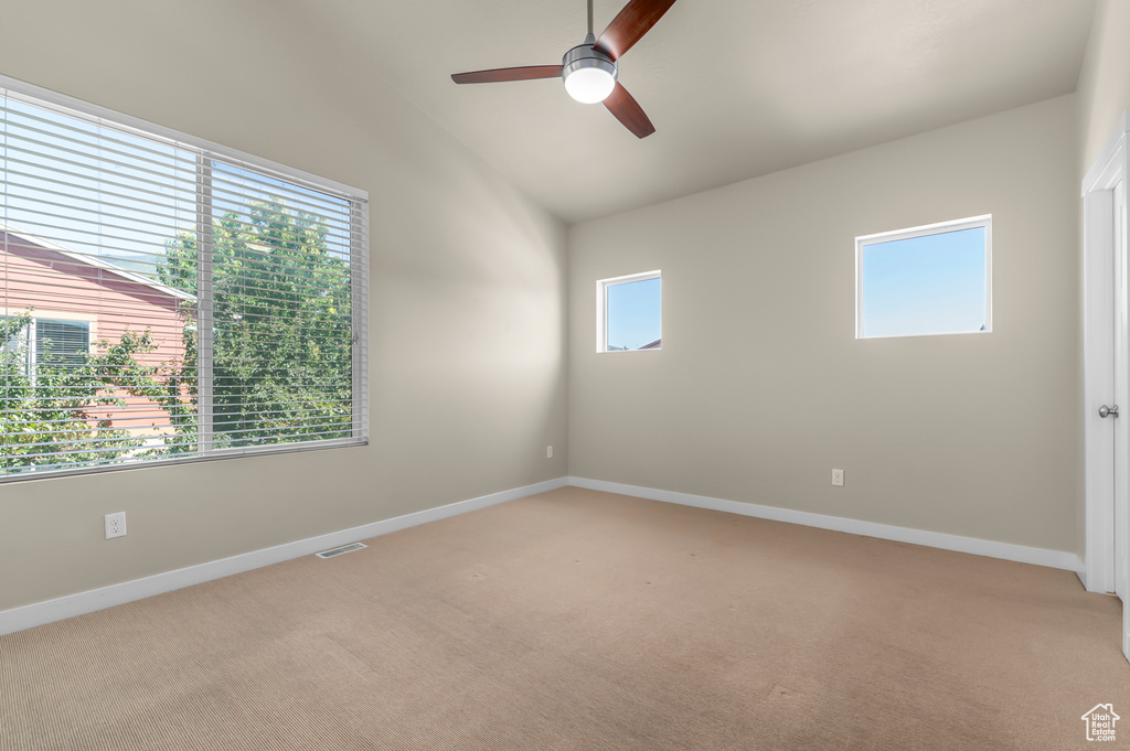 Empty room featuring light colored carpet, a ceiling fan, and vaulted ceiling