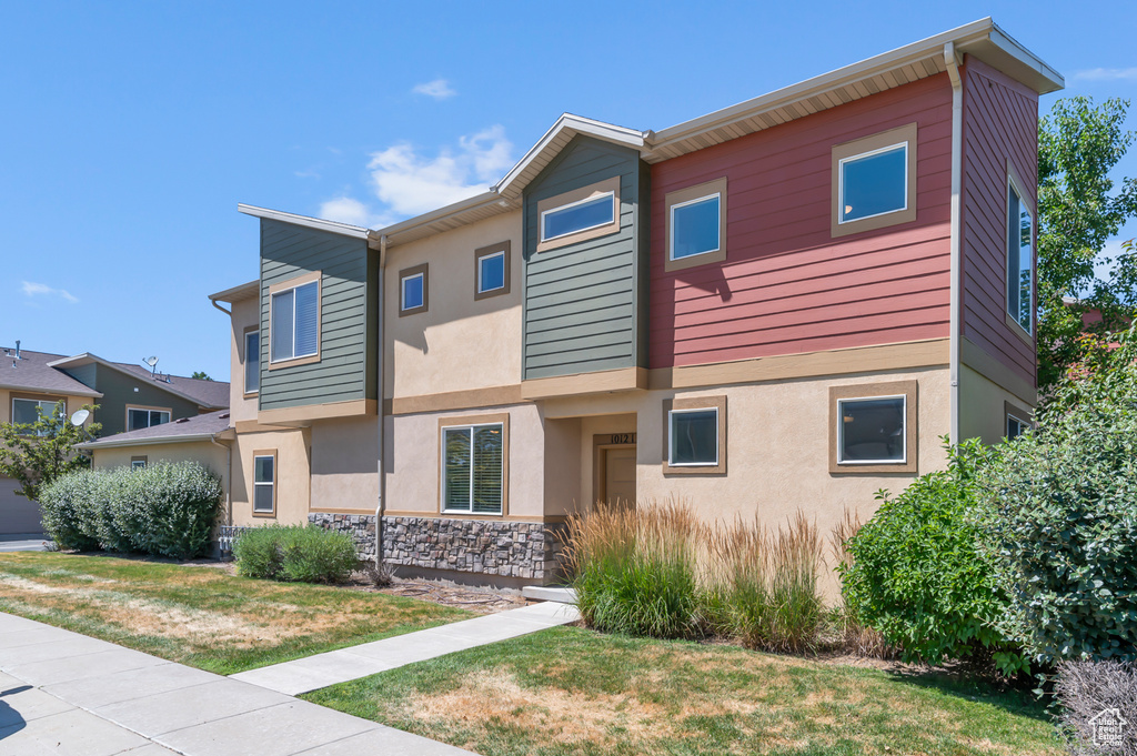 View of front of home featuring stone siding, stucco siding, and a front yard