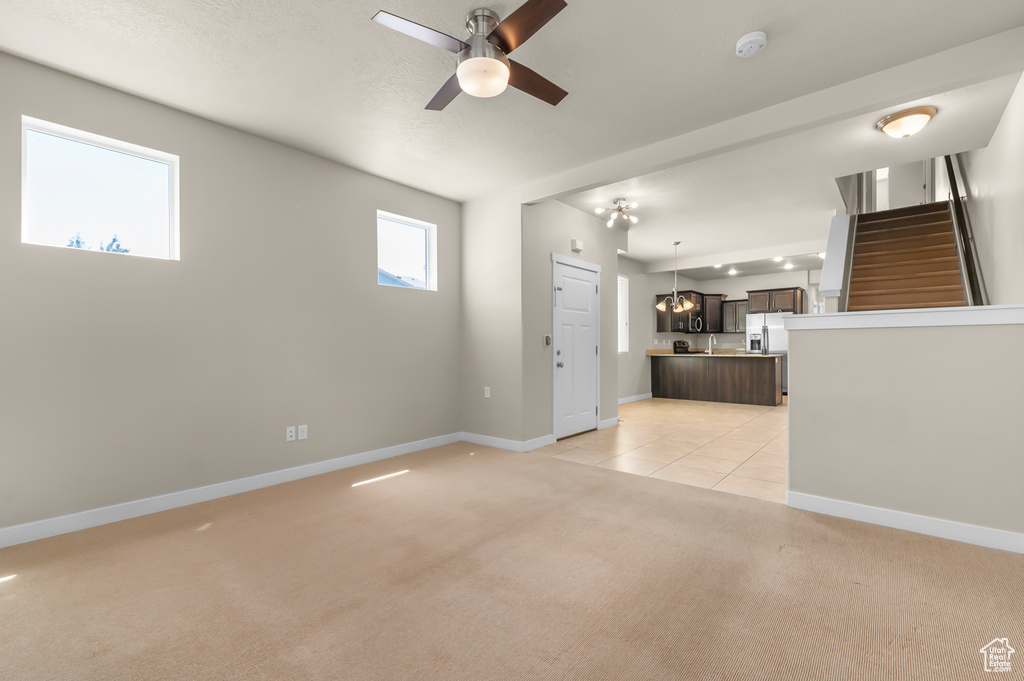 Unfurnished living room with light colored carpet, stairway, and a ceiling fan
