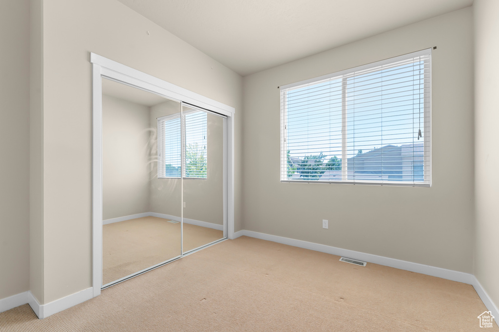 Unfurnished bedroom with carpet flooring, multiple windows, and a closet