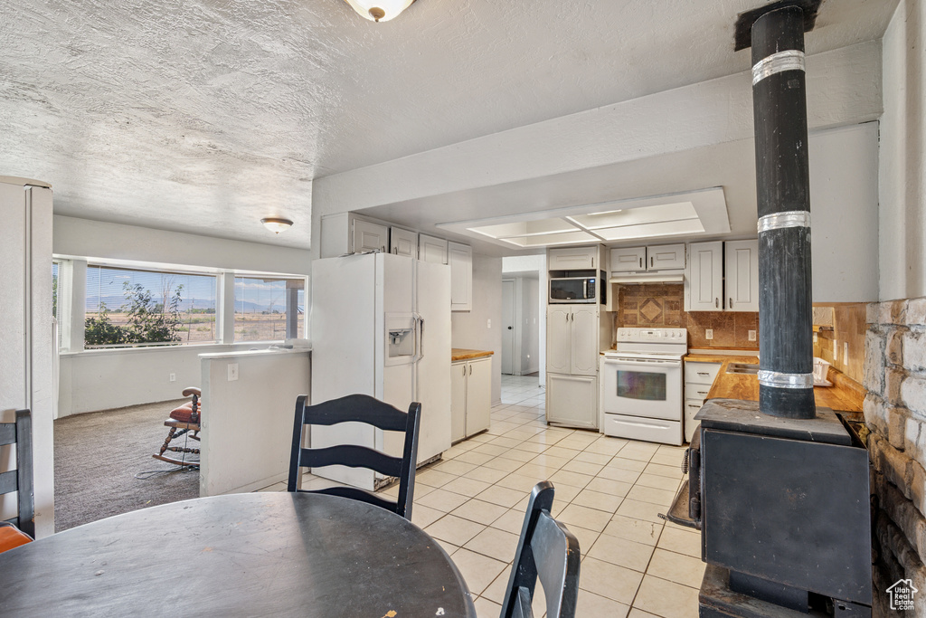 Kitchen with white appliances, a wood stove, light tile patterned floors, tasteful backsplash, and a textured ceiling