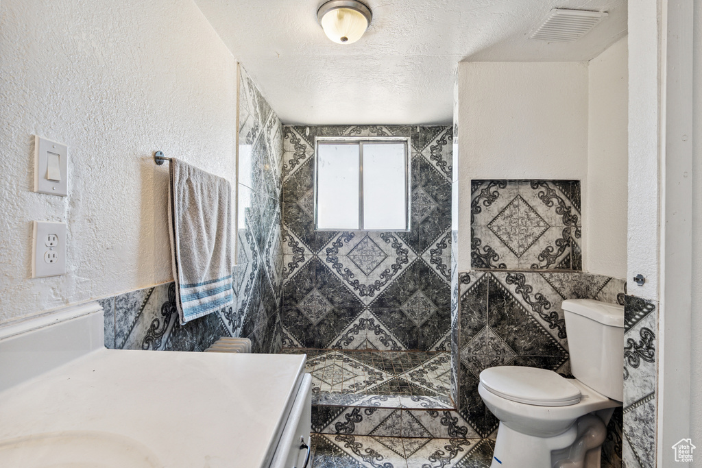 Full bathroom featuring tiled shower, vanity, a textured wall, a textured ceiling, and tile walls