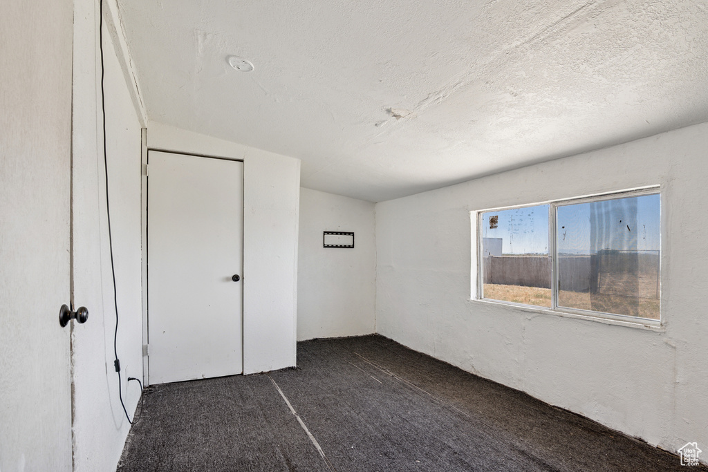 Unfurnished bedroom with dark colored carpet, a closet, and a textured ceiling