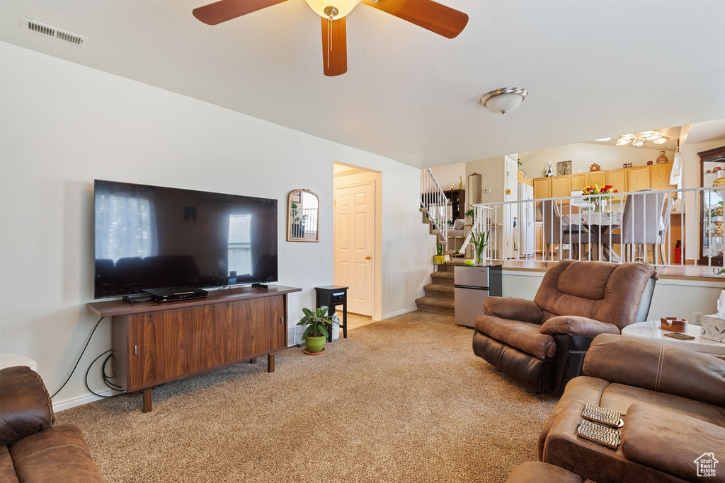 Living area featuring light carpet, stairs, and a ceiling fan