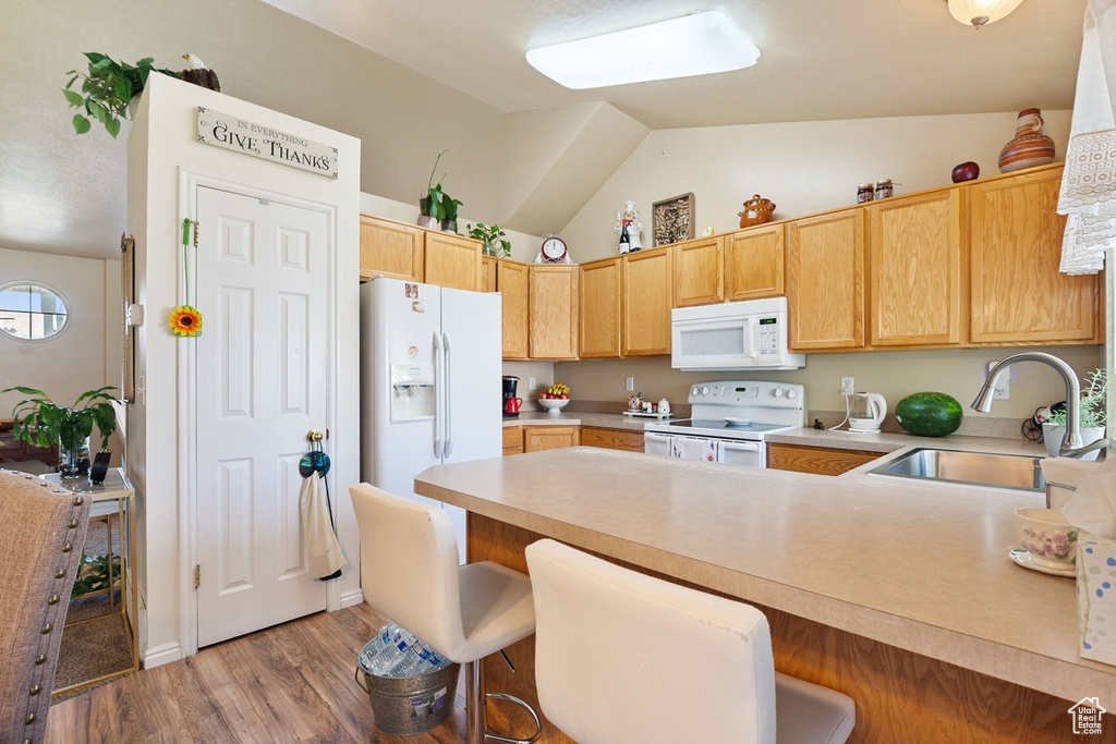 Kitchen with white appliances, lofted ceiling, a peninsula, light countertops, and light wood finished floors