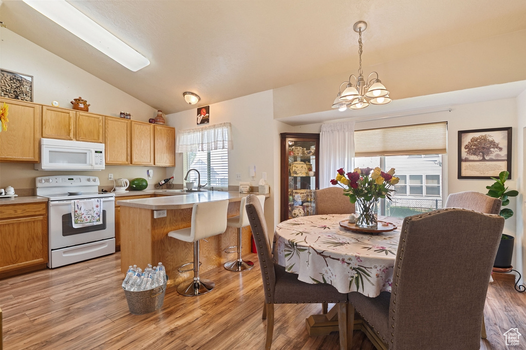 Kitchen with white appliances, vaulted ceiling, light countertops, a chandelier, and a kitchen breakfast bar