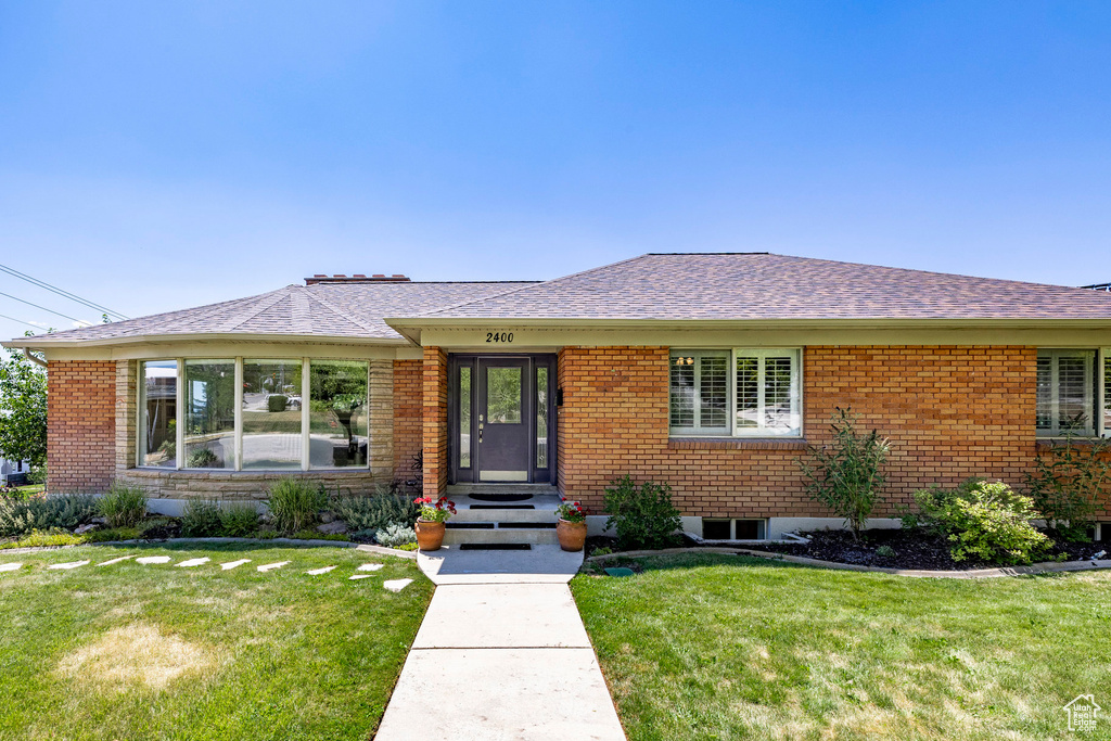 View of front of property featuring a front lawn, brick siding, and roof with shingles