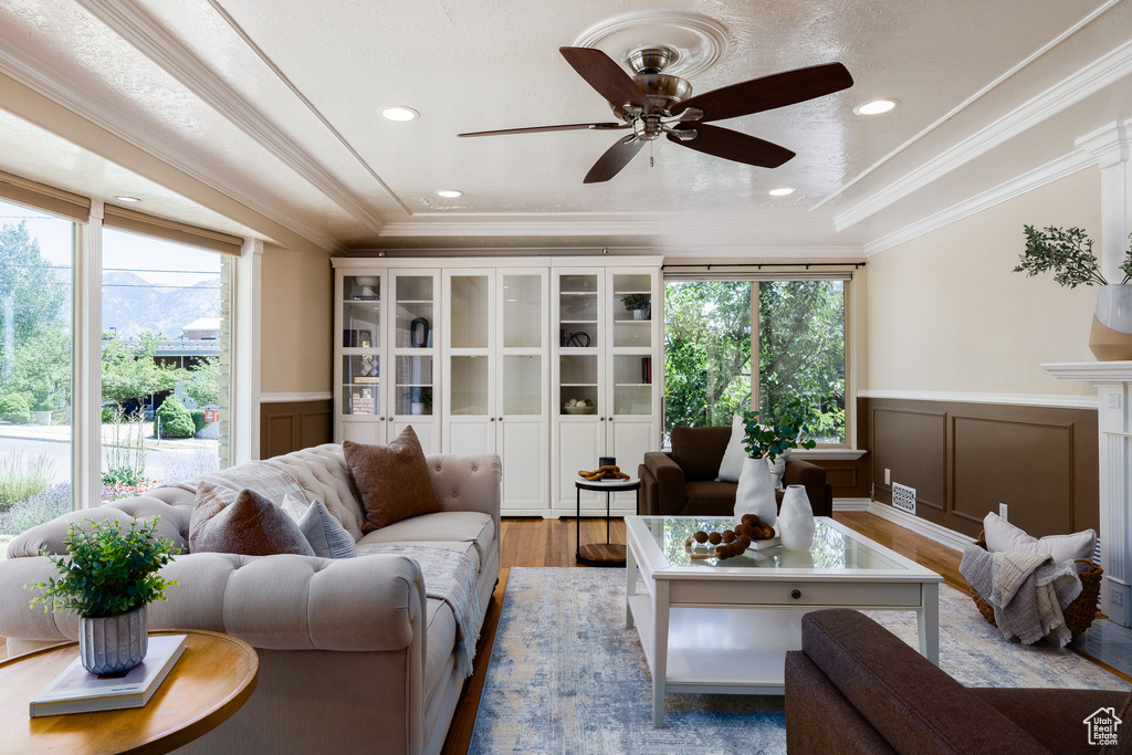 Living area with a decorative wall, wood finished floors, a wainscoted wall, ornamental molding, and a ceiling fan