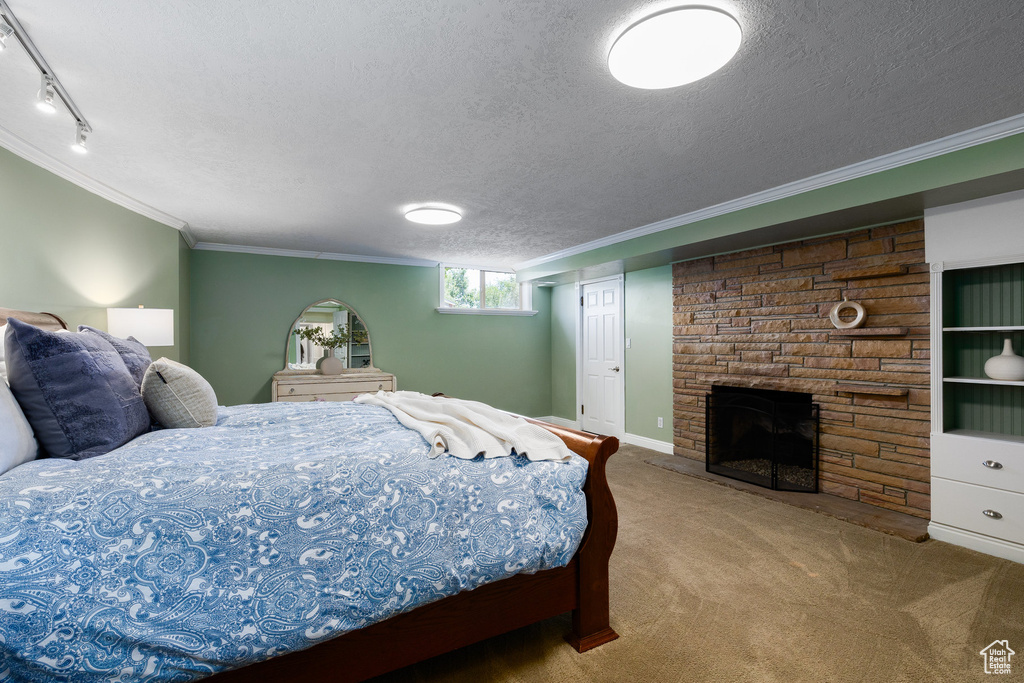 Carpeted bedroom with crown molding, a textured ceiling, a fireplace, and rail lighting