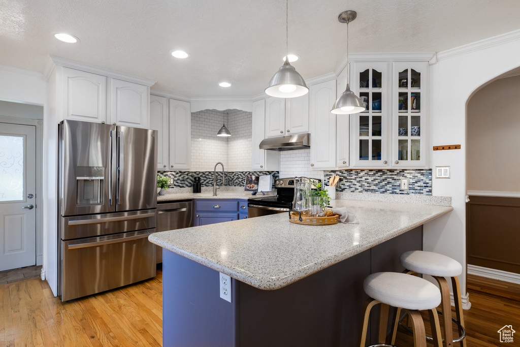 Kitchen featuring stainless steel appliances, under cabinet range hood, a peninsula, a kitchen bar, and white cabinets