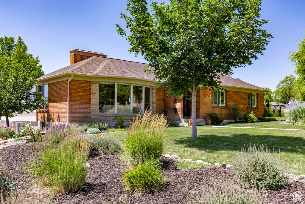 Ranch-style house with brick siding, a chimney, a front lawn, and roof with shingles