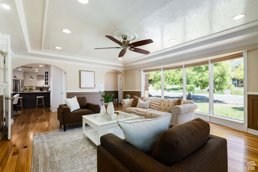 Living room featuring arched walkways, plenty of natural light, wainscoting, a ceiling fan, and ornamental molding