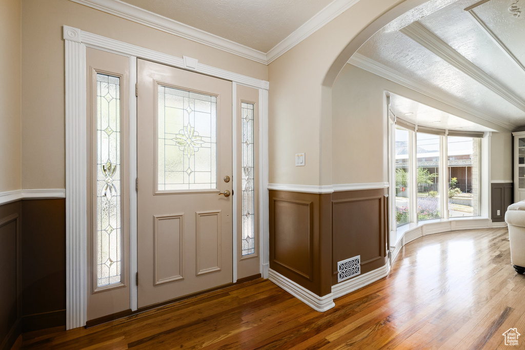 Foyer entrance with arched walkways, ornamental molding, wood finished floors, a decorative wall, and a wainscoted wall
