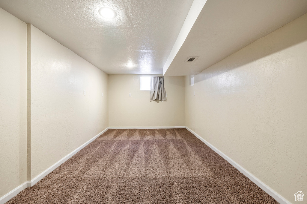 Below grade area with carpet, a textured ceiling, and a textured wall